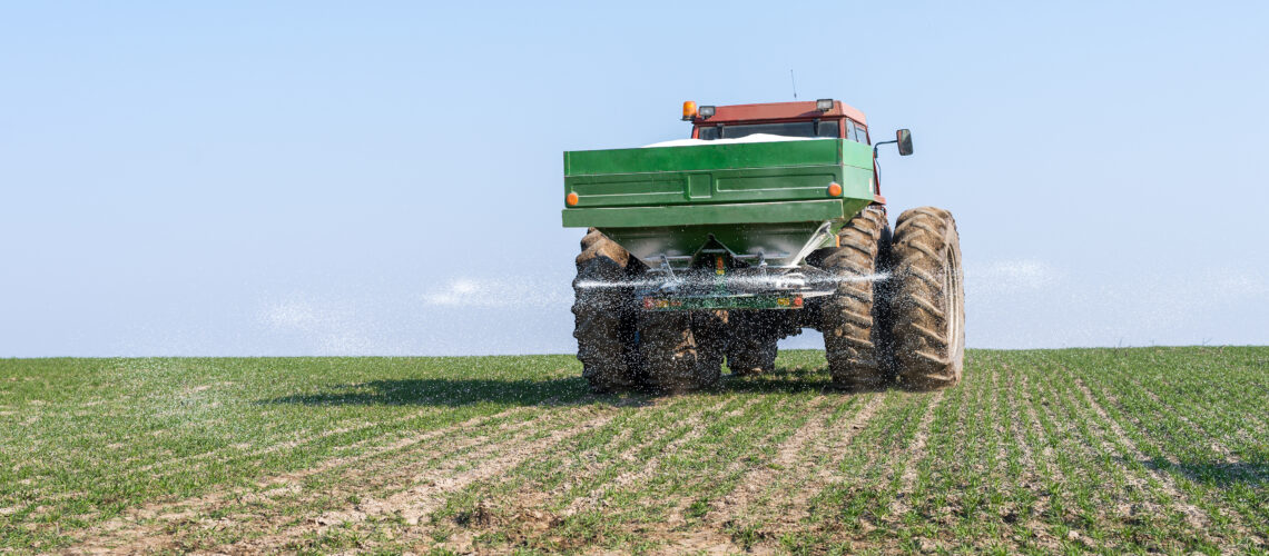 Tractor and fertilizer spreader in field.