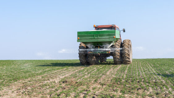 Tractor and fertilizer spreader in field.