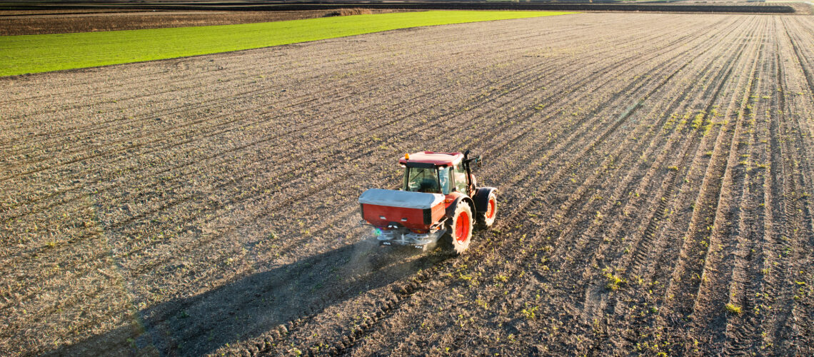 Tractor spreading artificial fertilizers in field.