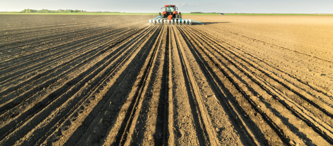 Farmer with tractor seeding soy crops at agricultural field.