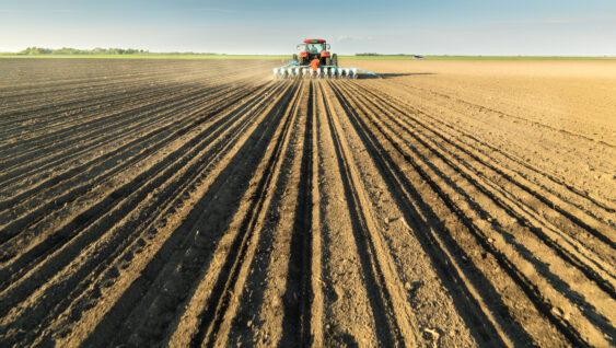 Farmer with tractor seeding soy crops at agricultural field.