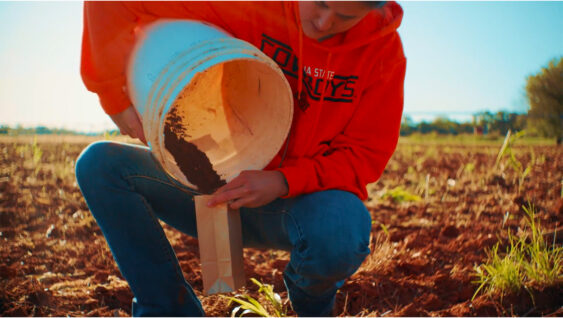 A farmer in a field pouring soil into a bag.