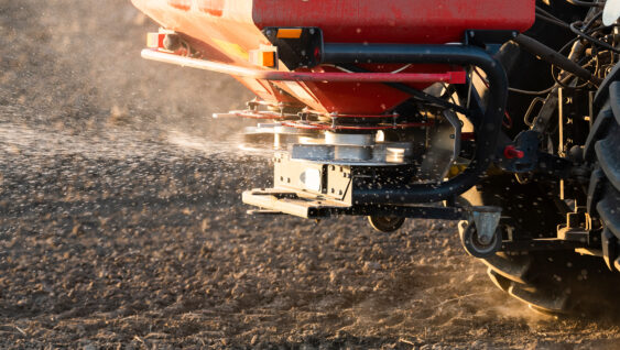 Tractor spreading artificial fertilizers in field.