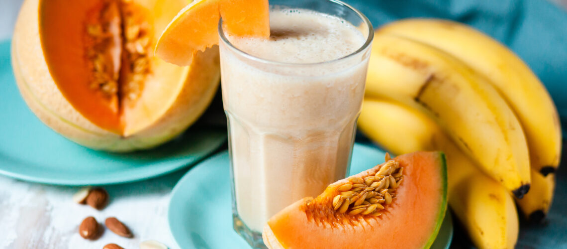 A cut open cantaloupe, a bunch of bananas, and a smoothie.