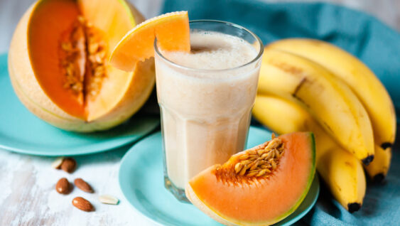 A cut open cantaloupe, a bunch of bananas, and a smoothie.