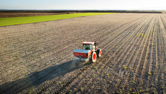 Tractor spreading artificial fertilizers in field.