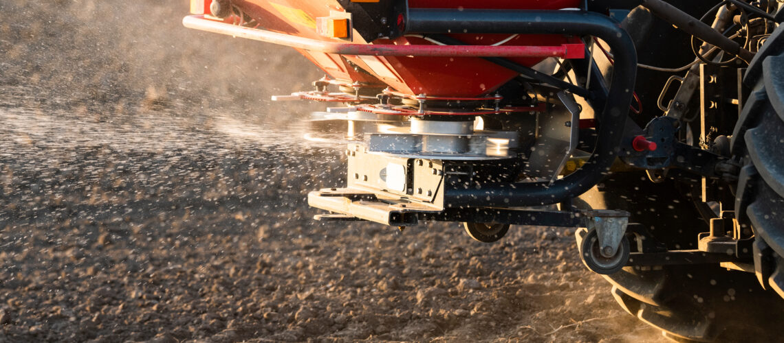 Tractor spreading artificial fertilizers in field.