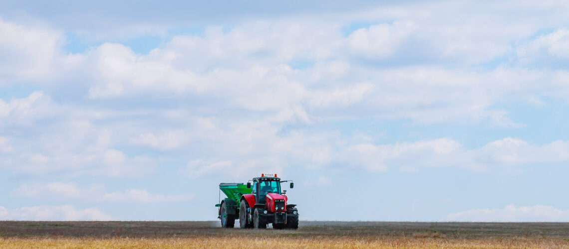 A red tractor in a green trailer is carrying fertilizer to the field. Agricultural work is performed by a farmer.