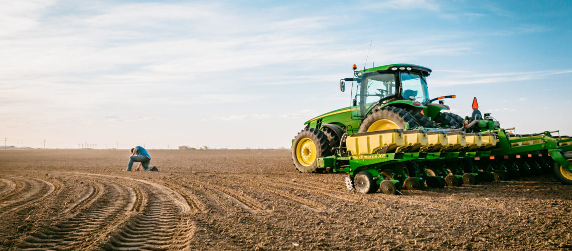 farmer checking soil while planting, green planter sitting in farm field