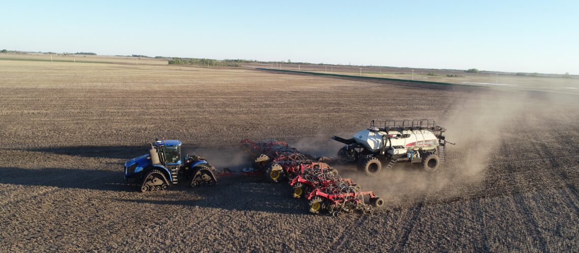 blue tractor pulling seeder and fertilizer bin in spring to place fertilizer with the seed