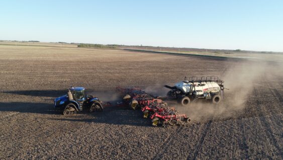blue tractor pulling seeder and fertilizer bin in spring to place fertilizer with the seed