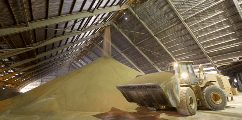 A front-end loader moving a large pile of phosphate fertilizer granules inside a Nutrien storage facility, highlighting the scale and importance of phosphorus in global crop nutrition.